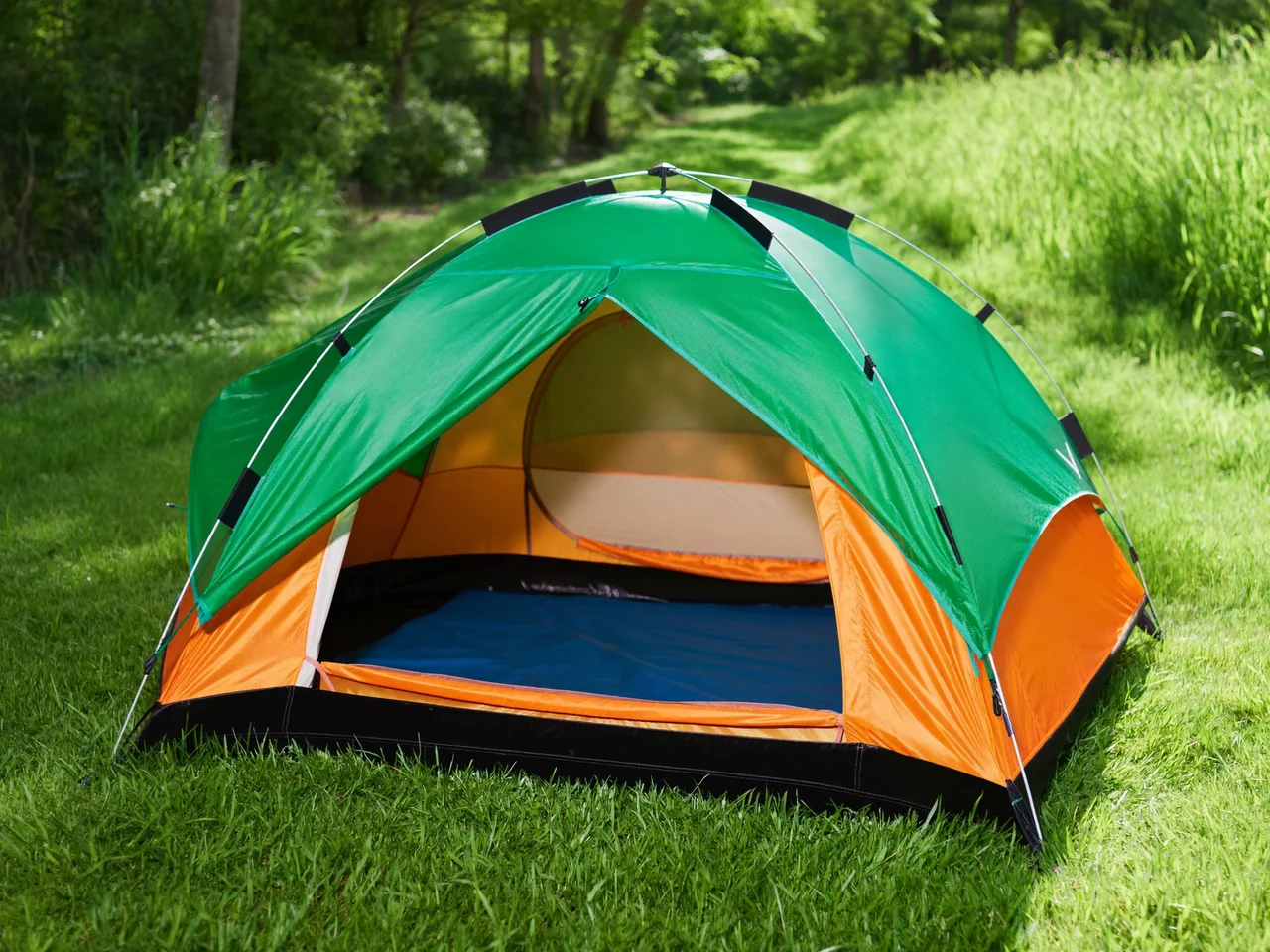 Tenda a cupola verde e arancione montata sull'erba, con la porta aperta