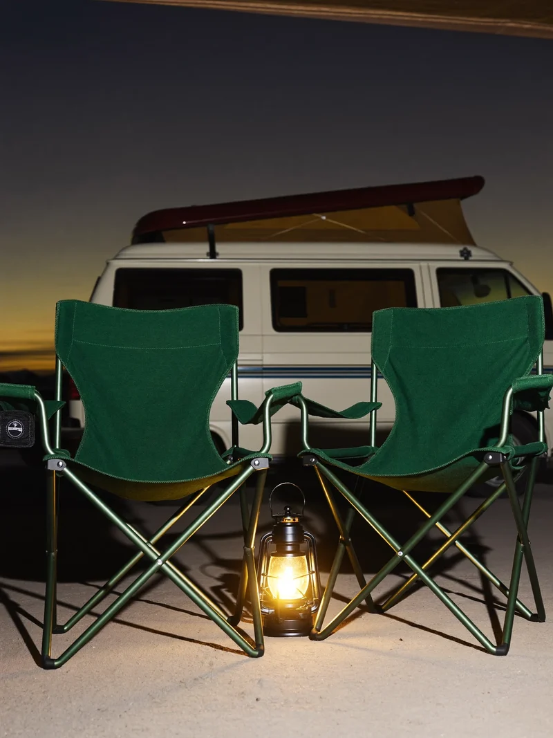 Due sedie pieghevoli e una lanterna accesa sotto la veranda di un camper al tramonto